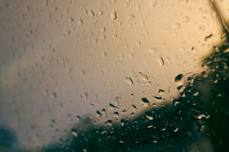 Water droplets on glass catch warm light and dark reflections.